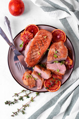 Roasted duck breast with blood oranges, thyme and onion served on the ceramic plate on the white table. Hot exquisite poultry meal. Top view
