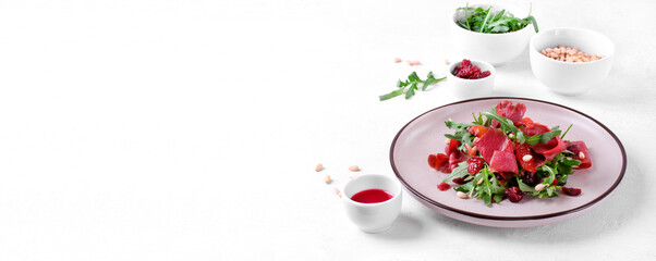 Obraz na płótnie Canvas Salad with smoked duck breast, arugula, dried cranberry, pine nuts and blood orange juice dressing served on the ceramic plate. Exquisite cold appetizer. Web banner with copy space on white