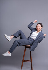 Young Asian businesswoman sitting on chair and posing on gray background