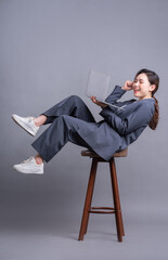 Young Asian businesswoman sitting on chair and using laptop on gray background
