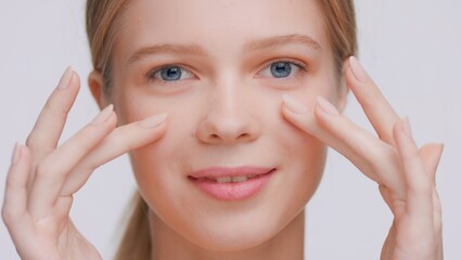 Extreme close-up beauty portrait of young woman who touches her face under eyes | Cream commercial concept.