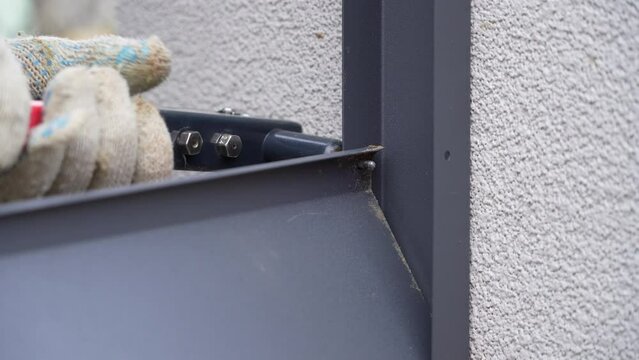 Close up shot on hands of man using rivet plier to join metal profiles to the fence rails. Handyman attaching metal parts of blinds fence with tool