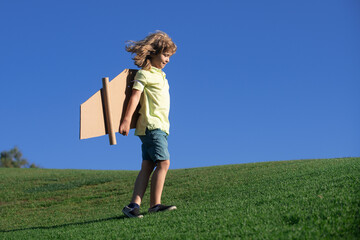 Portrait of cute blond child play pilot with handmade craft paper plane wings. Kids dreaming, success, creative and startup concept. Copy space for text.