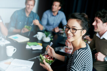 Enjoying a team lunch. Portrait of a young office worker eating lunch with coworkers at a boardroom table.