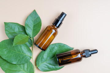 Amber glass cosmetic bottles with a dropper on a beige background with tropical leaves. Natural cosmetics concept, natural essential oil and skin care products.