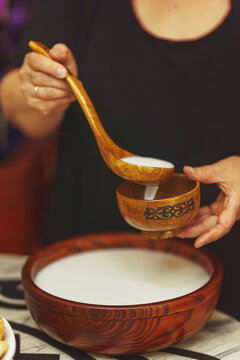 A woman pours "kumis" milk drink into a wooden bowl with an ornament in the national Kazakh style. Central Asian traditional drink on the festive table Nauryz.