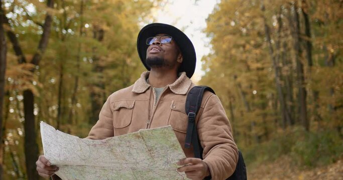 Young black tourist with a map in the autumn forest