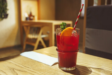 Cocktail in a transparent glass with a straw and ice close-up. Red drink with mint and orange on the table in the cafe real photo. Iced tea mors lemonade in a glass © Yashkin Ilya