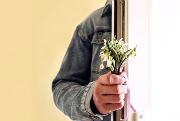 Snowdrops - romantic spring gifts: a bouquet of snowdrops in the hand of a young man hiding behind a door, space for text