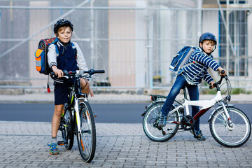 Two school kid boys in safety helmet riding with bike in the city with backpacks. Happy children in colorful clothes biking on bicycles on way to school. Safe way for kids outdoors to school