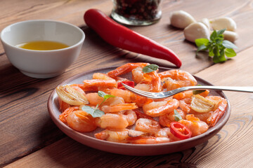 Close-up view of shrimps pinchos tapas from Spain in plate with fork, red pepper, garlic, oil on on wooden rustic background. Selective focus.