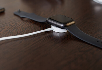 The black watch is on charge, wireless charging of the wristwatch gadget - obrazy, fototapety, plakaty