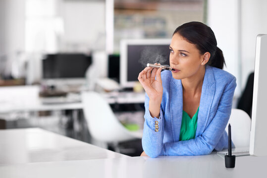 Having a quick vape between meetings. Shot of a businesswoman smoking and electronic cigarette in an office.