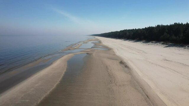 Morze Bałtyckie, widok z lotu ptaka z drona lecącego nad pustą, piękną plażą. Drobne fale rozbijające się o piaszczystą plażę.