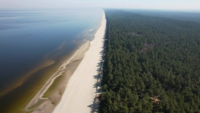 Morze Bałtyckie, widok z lotu ptaka z drona lecącego nad pustą, piękną plażą. Drobne fale rozbijające się o piaszczystą plażę.
