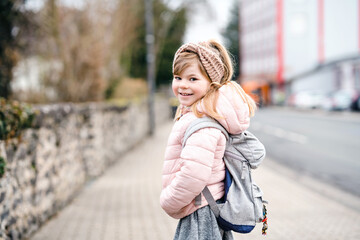 Cute little preschool girl going to playschool. Healthy toddler child walking to nursery school and kindergarten. Happy child with backpack on the city street, outdoors.