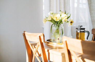 Beautiful bouquet of yellow tulips in vase on dinner table in the white kitchen light interior at home