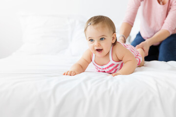 Baby lying on white bed with mother pulling on her feet