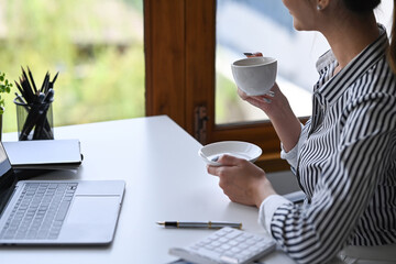 Relaxed businesswoman enjoy coffee break and looking out of the office window.
