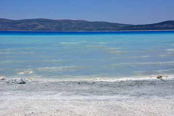 salda lake with white and gray sand and light blue water with mountains on background