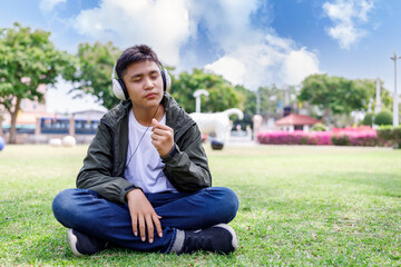 teenage student boy sitting on grren grass and listen to music with headphone relax in the lawn, park ,summer student concept,.