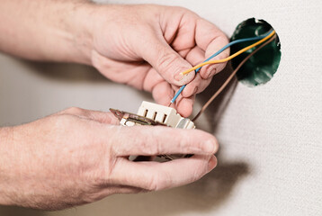 Assembly of the electrical network in the room. Installation of the electrical network, selective focus on hands. Electrician installing light switch in home.