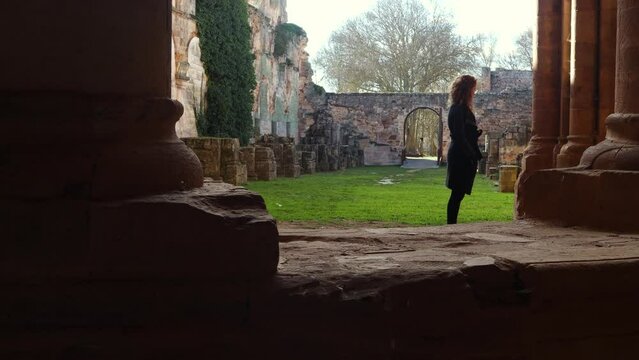 Young redhead girl admiring the ruins of a monastery in Spain. XII-XIII century buiding of the christian monastic cluny order, female traveler. Woman exploring ancient ruins.