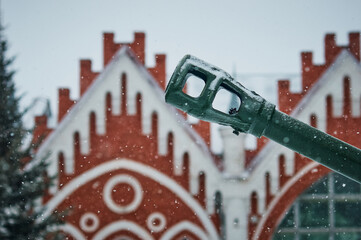 The barrel of an artillery gun during a snowfall. The contours of buildings and trees are blurred...