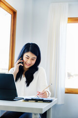 business dealings, an Asian company secretary is on the phone with customers comes to contact with using pen to write down the time to summarize the schedule for work the owner of the company.