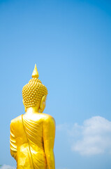 A back of gold buddha statue standing isolated on blue sky background.
