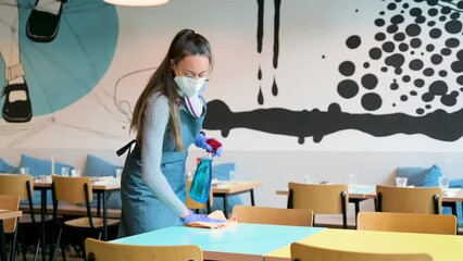 Waitress with protective face mask and apron sanitizing table in restaurant. Cleaning, health and pandemic concept.