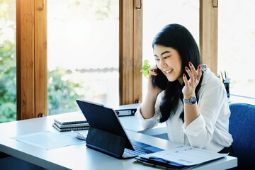 A female entrepreneur or businesswoman shows a smiling face while using smartphone and tablet computer for video conference working on a wooden table.