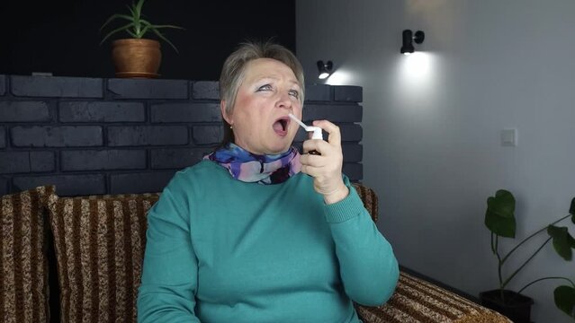 Sore throat. An elderly woman treats her mouth with medicine. The use of a local antiseptic. Treatment of sore throats, flu and colds. Inhalation.