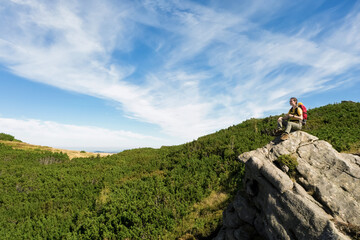 Young woman with backpack on rocky cliff in mountains