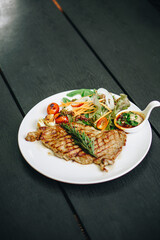 Pork steak with lettuce in white plate on black wooden table