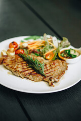 Pork steak with lettuce in white plate on black wooden table