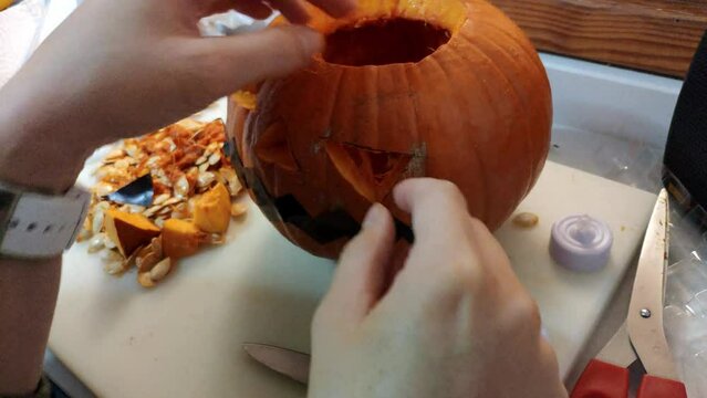 Pumking being carved to make a jack-o'-lantern for Halloween. Female and kids hand remove pieces of the pumking with the shape of the eyes. Some scissors are used to remove pieces and fibre.