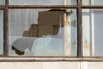 A broken window in a metal frame.Rusty metal frames on the window.Dirty, broken windows.Devastation, vandalism.