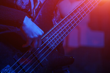 Obraz na płótnie Canvas The bass guitarist plays the bass guitar in the spotlight. Selective focus