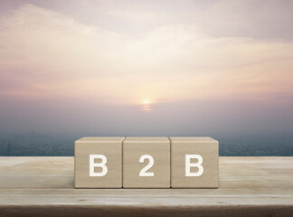 B2B acronym on wood block cubes on wooden table over city tower and skyscraper at sunset, vintage style, Business to business marketing and strategy concept