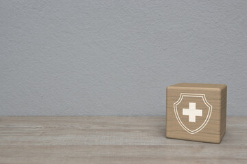 Cross shape with shield flat icon on wood block cube on wooden table over white wall background, Business healthy and medical care insurance concept