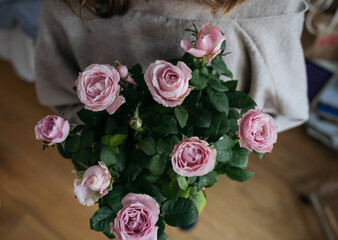 High view of a young woman holding a flower pot with pink rose bush