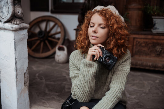 A woman in a beret and a green sweater holds a camera in her hands and takes shoots