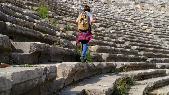 walk in Antalya Turkey on warm October afternoon. Pretty tourist woman with backpack at ruins of ancient city of Perge, large ancient amphitheater. walks on terraces of theater