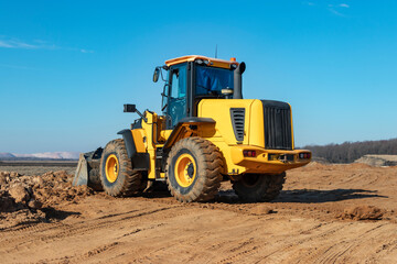 Bulldozer or loader moves the earth at the construction site against the blue sky. An earthmoving machine is leveling the site. Construction heavy equipment for earthworks.