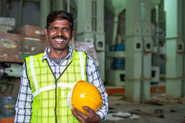Portrait of happy smiling industrial worer with safety helmet in hand looking at with copy space -...