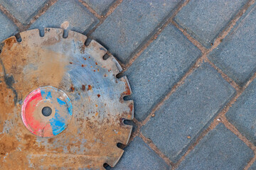 An old rusty metal cut-off wheel rests on the paving slabs. Close-up. Used construction tool.