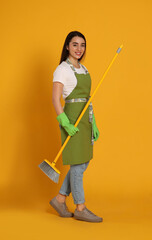 Beautiful young woman with broom on yellow background