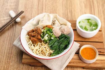 Mie ayam (noodles with chicken, meatballs, dumplings and vegetables) is a popular street food in Indonesia. Served in bowl on wooden table. Selective focus image, blurred background. Close up.
