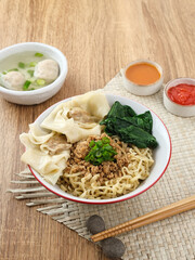 Mie ayam (noodles with chicken, meatballs, dumplings and vegetables) is a popular street food in Indonesia. Served in bowl on wooden table. Selective focus image, blurred background. Close up.
